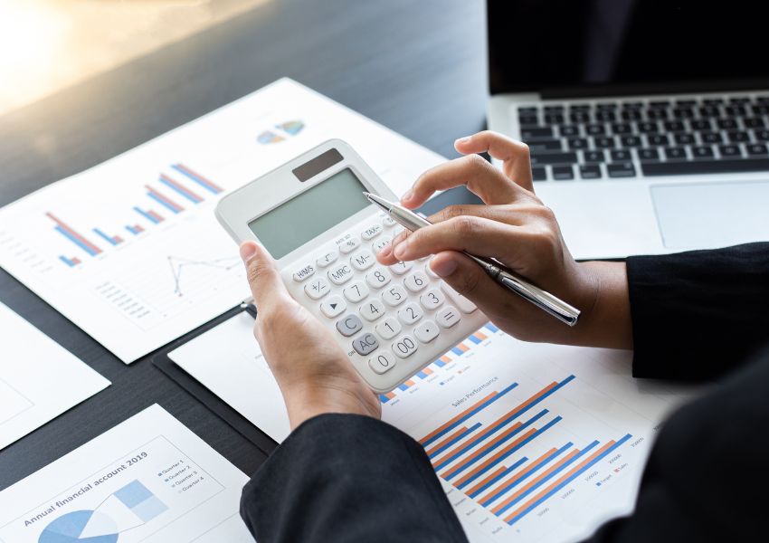 person holding a calculator with documents and graphs spread out on their desk